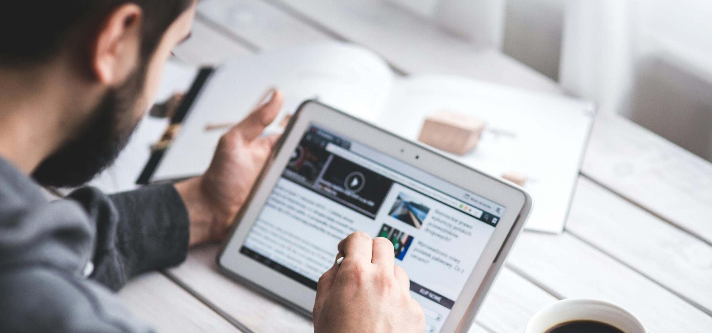 A man uses a tablet to browse news while enjoying a cup of coffee, stylus in hand.