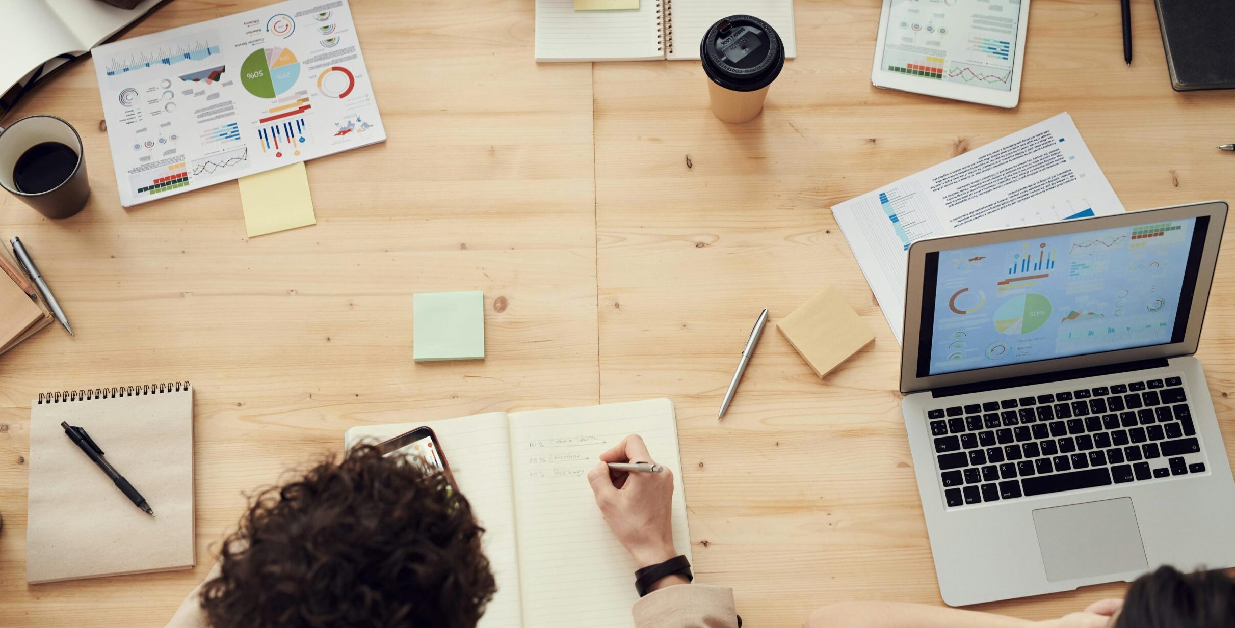 Business professionals in a collaborative team meeting, discussing charts and plans with laptops and notebooks.